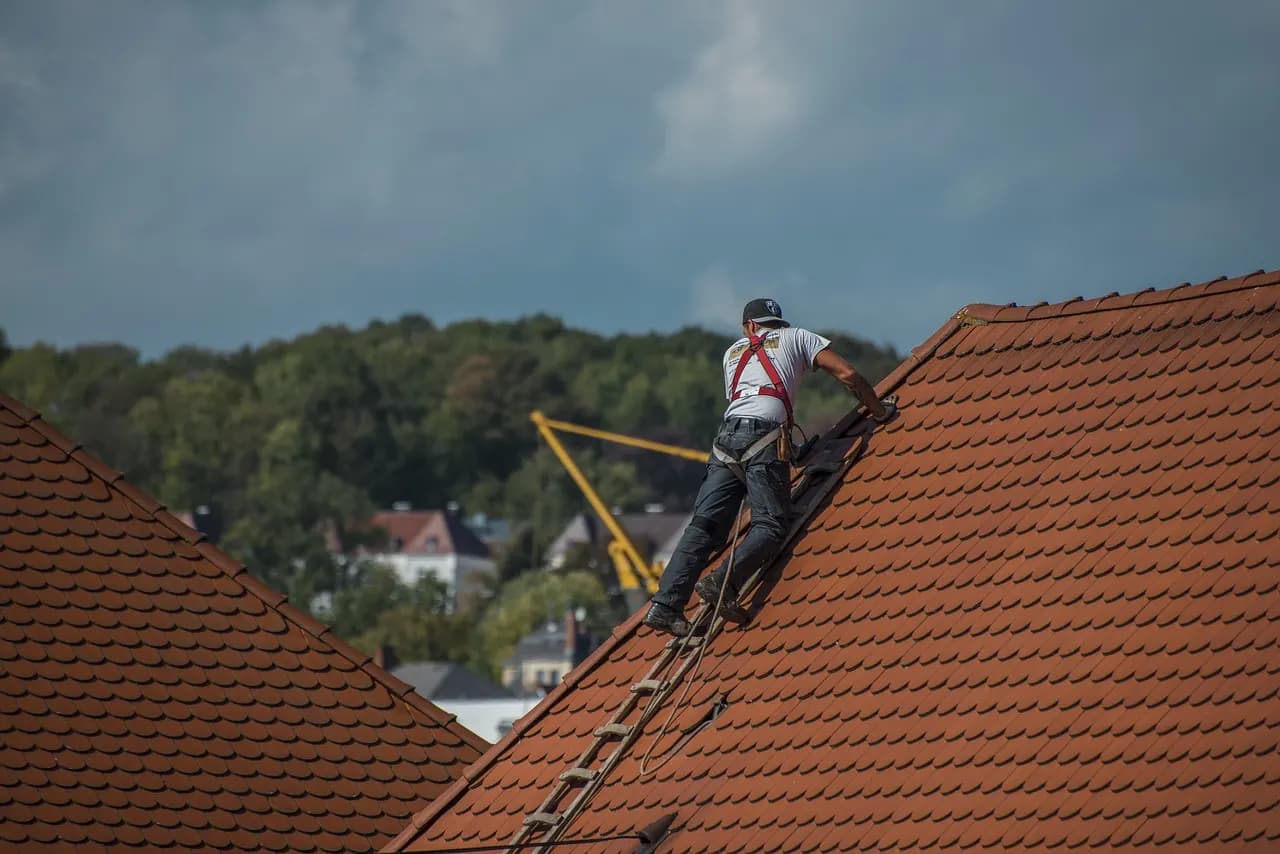 Couvreur sécurisé par harnais sur une toiture en tuiles